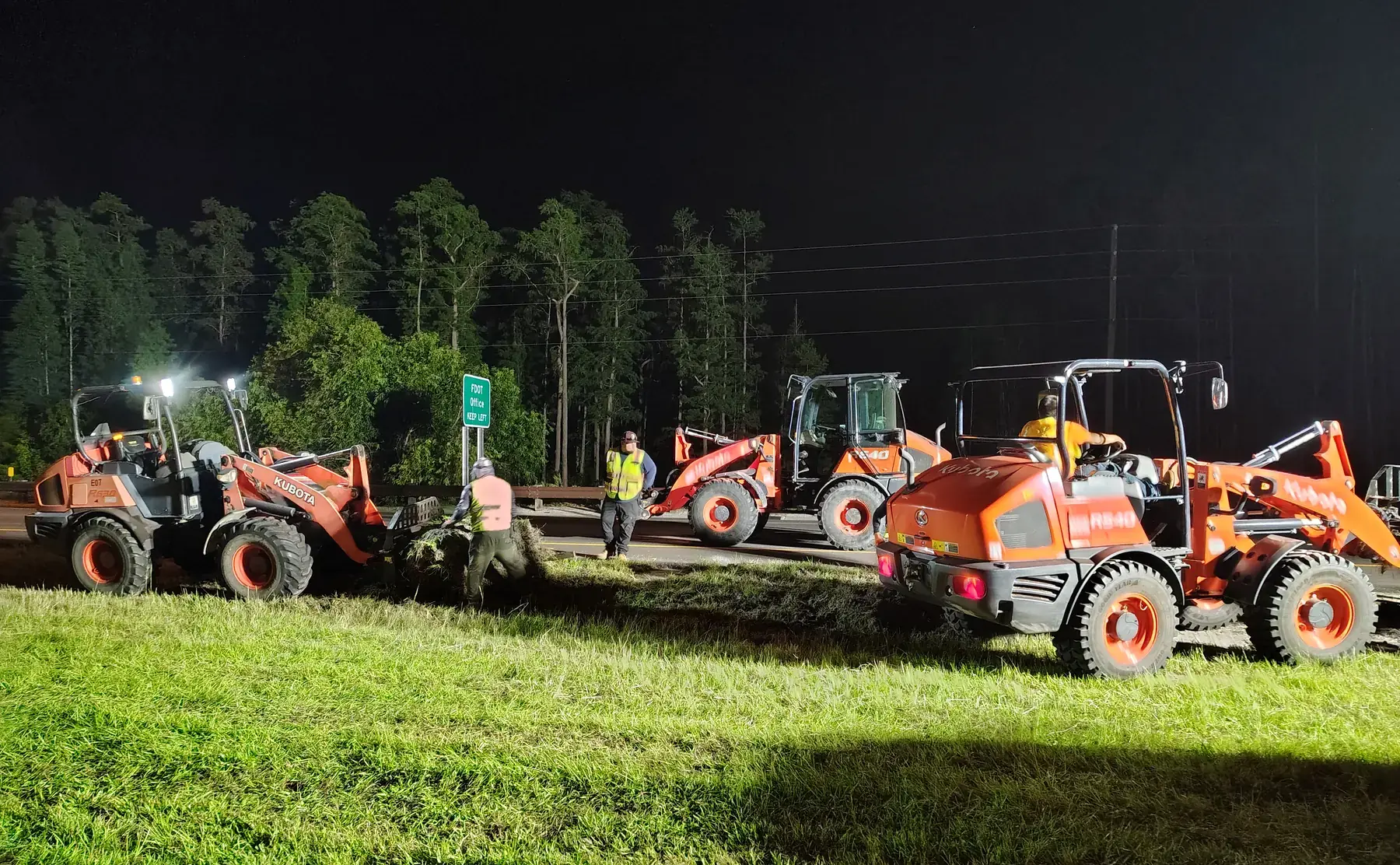 Turf installation equipment lined up in a lighted highway work area at night