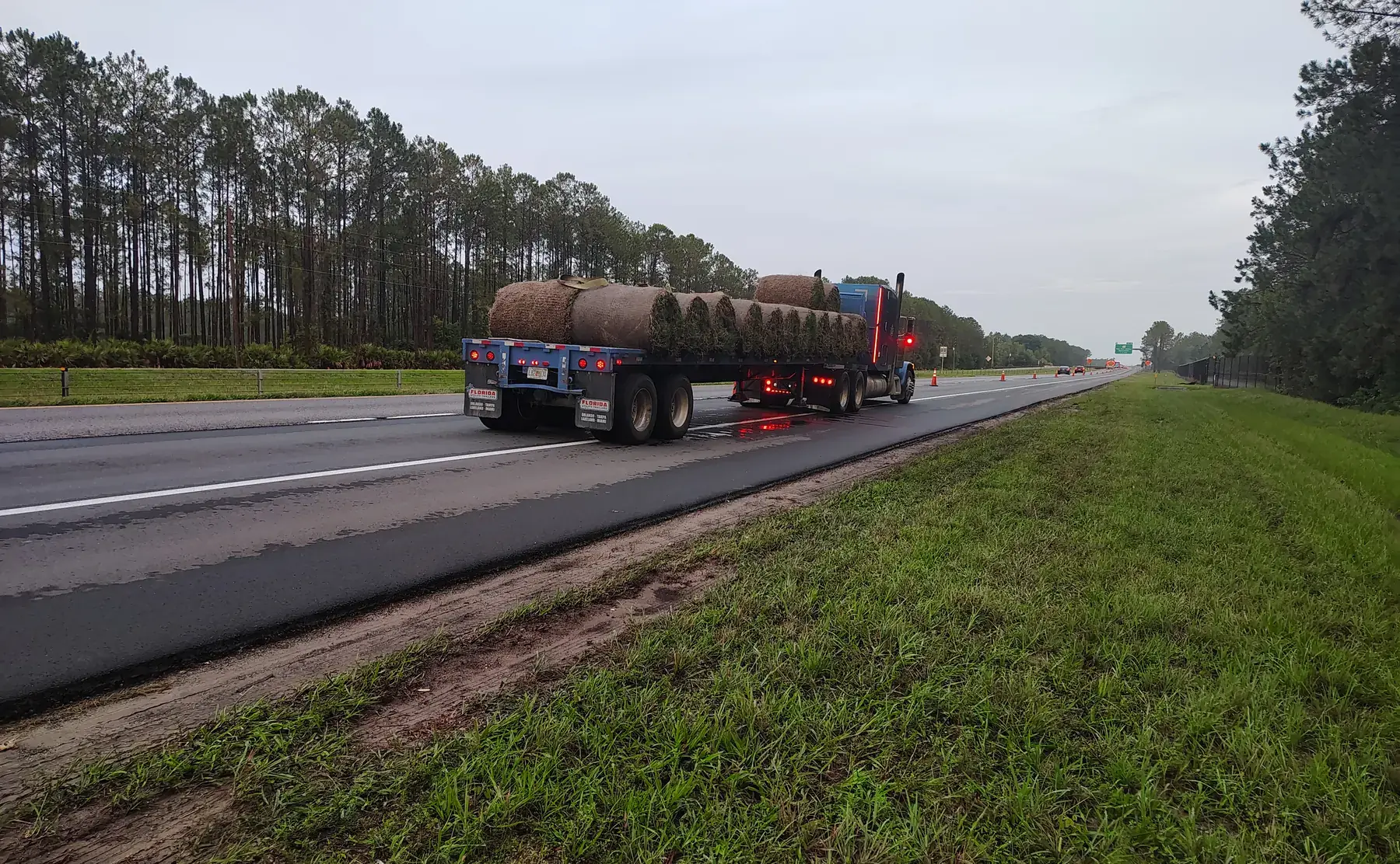 Flatbed truck carrying large sod rolls along a divided Pasco County toll-road work area